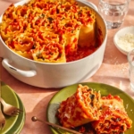 A plate with a serving of two lasagna roll ups and a baking dish with more in the background.