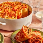 Lasagna roll ups in a baking dish with some servied onto a plate next to it.