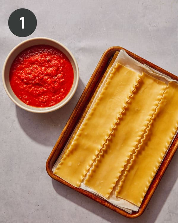 Cooked lasagna sheets with parchment between them on a baking sheet.