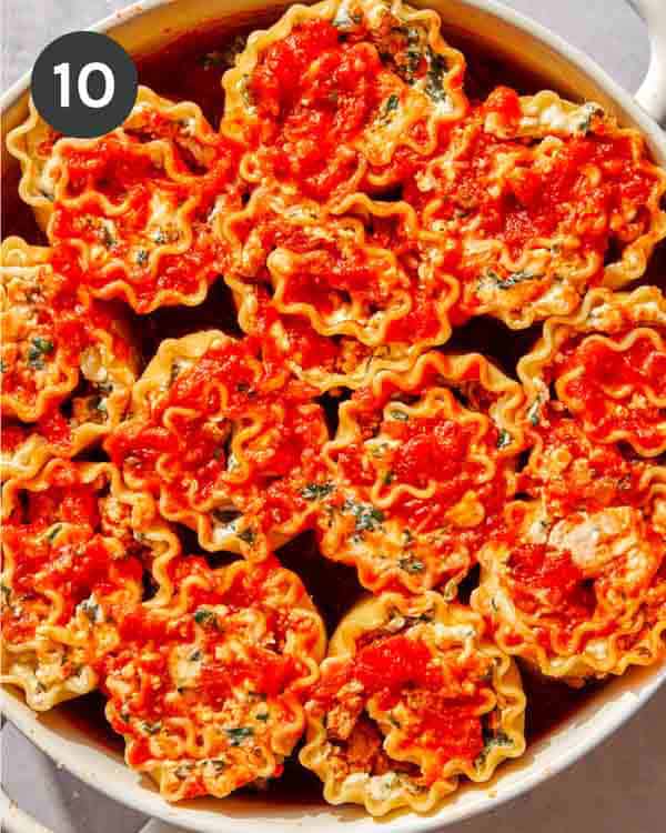 A baking dish with lasagna roll ups in it and some marinara on top.