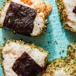 Close up on spicy tuna onigiri with one dipped in masaga sauce.