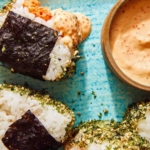 Close up on spicy tuna onigiri with one dipped in masaga sauce.