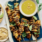 Chicken satay on a platter with lime wedges.