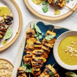 Chicken satay on a platter with lime wedges.