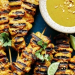 Chicken satay on a platter with lime wedges.