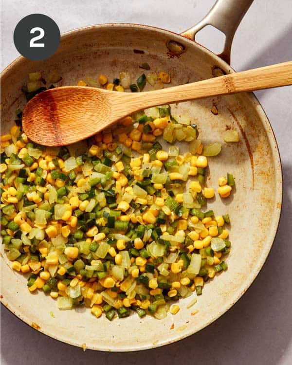 An onion and pepper mixture with corn in a skillet cooking.