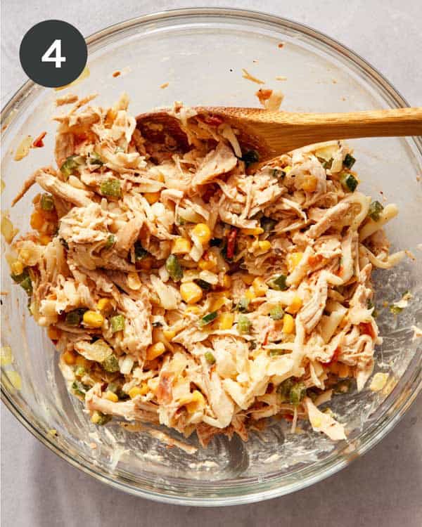 Shredded chicken mixed with onion, corn, poblano, salsa, and sour cream in a bowl.