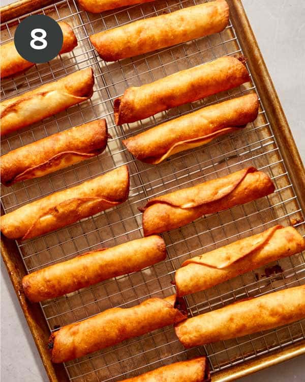 Freshly fried flautas on a sheet pan resting.