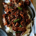 Mongolian Beef on a platter over rice with a spoon in it.