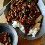 Mongolian Beef on a platter over rice with a spoon in it.