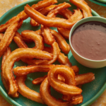 Spanish Churros on a plate with a bowl of chocolate sauce on the side.