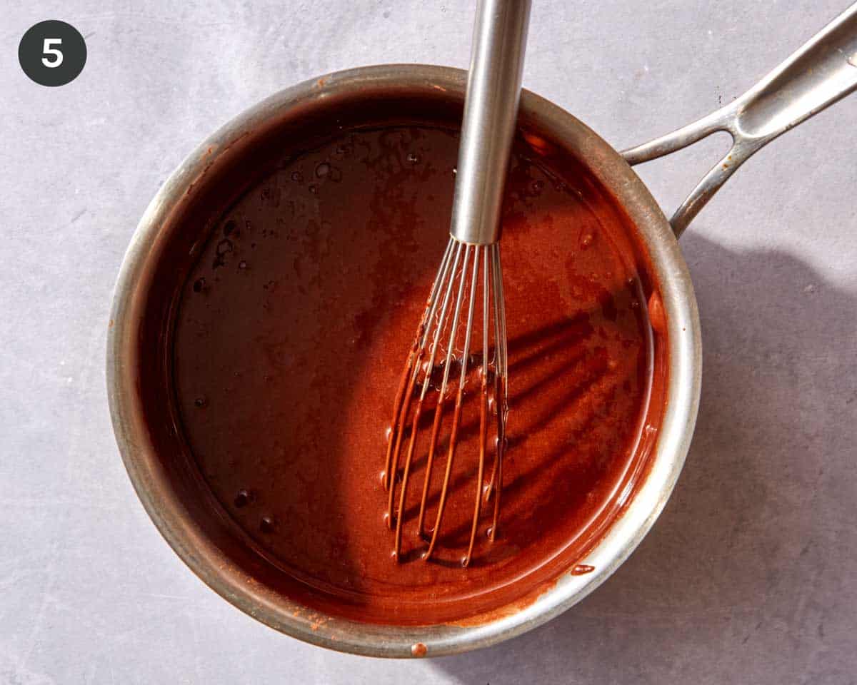 A pot full of freshly made homemade chocolate sauce with a whisk in it.