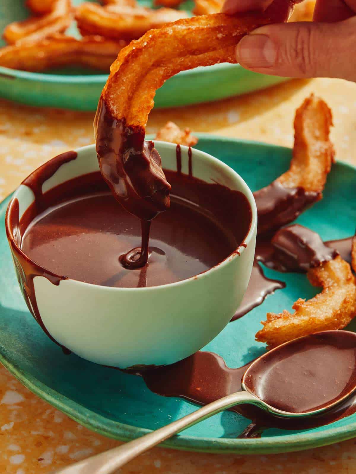 A bowl of homemade chocolate sauce with a churro being dipped in it.