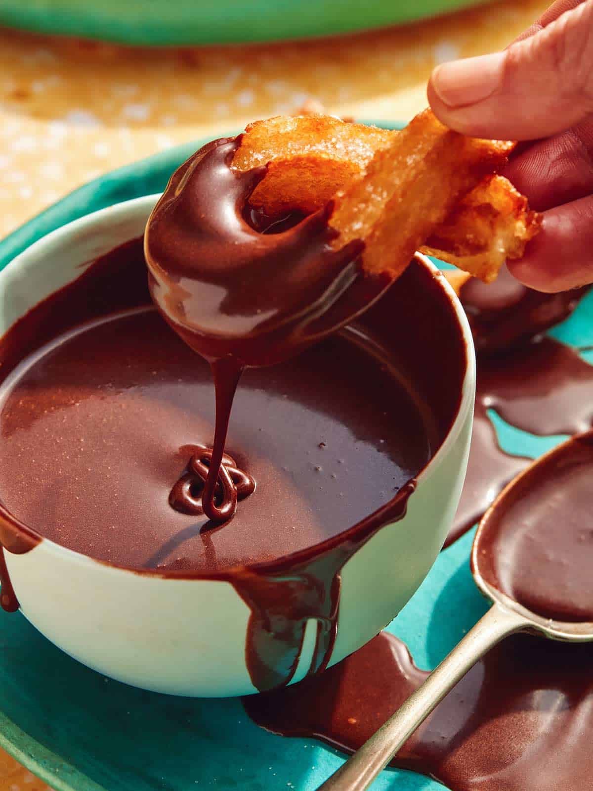 Close up on a bowl of chocolate sauce with a Spanish churro being dipped into it.