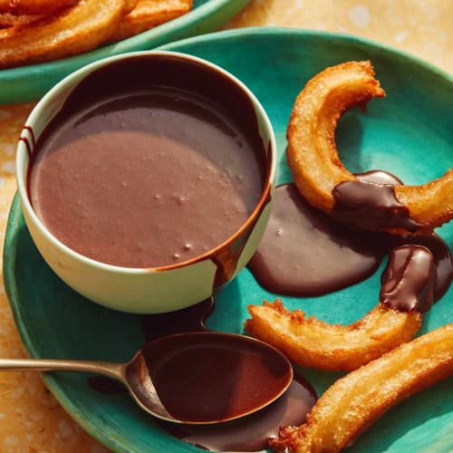 A plate with churros and a bowl of homemade chocolate sauce.