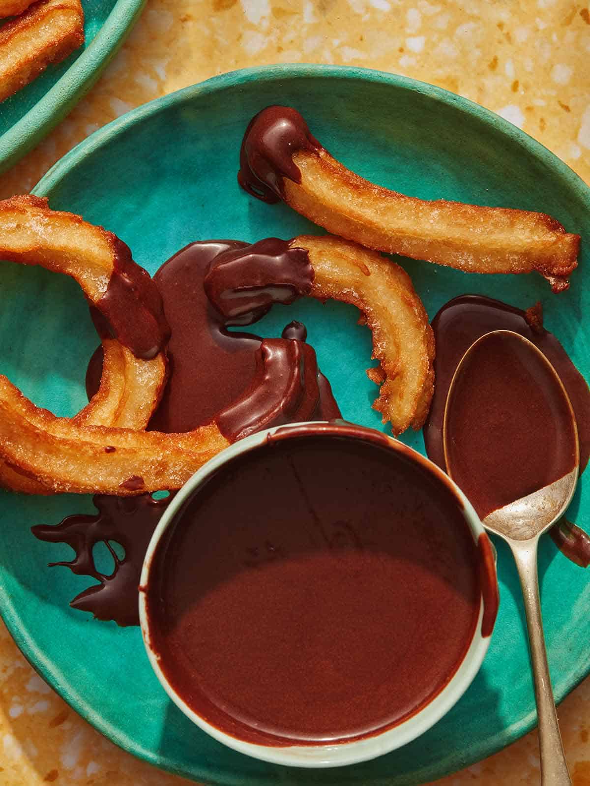 Overhead on a bowl of homemade chocolate sauce with a spoon and churros on the side.