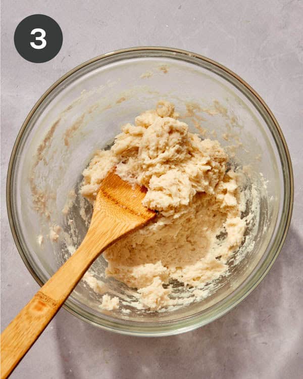 Spanish churro batter in a glass bowl with a wood spoon being mixed together.