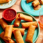 A platter of spring rolls with some being served on plates in the background.