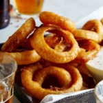 Beer battered fried onion rings with ranch dressing and beer on the side.