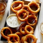 A serving of beer battered fried onion rings with ranch.