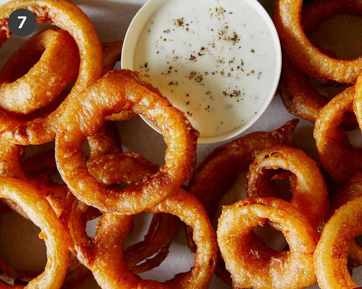 A platter of onion rings with ranch on the side.