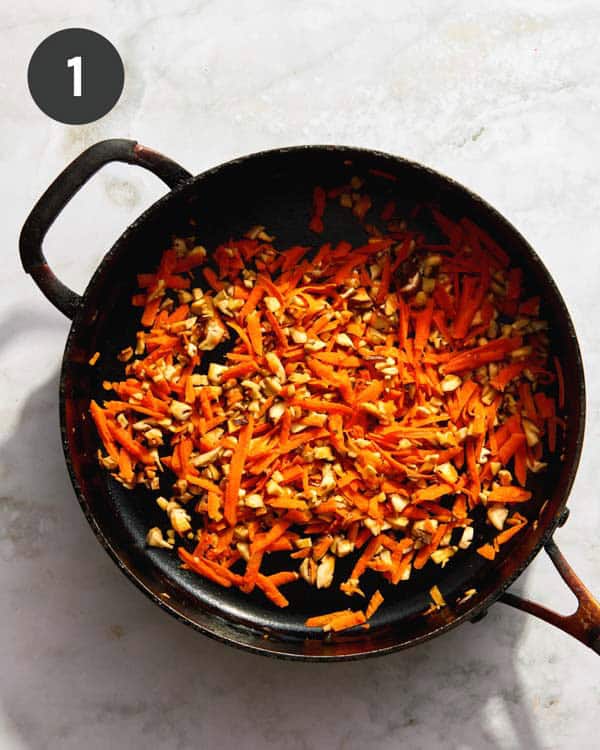 Carrot, garlic, and mushrooms being cooked in a skillet.