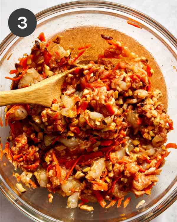 Filling ingredients mixed together for spring rolls in a bowl with a wooden spoon.