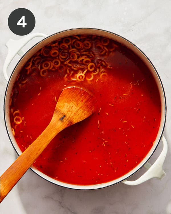Pasta being added with tomato paste and sauce in a pot simmering.