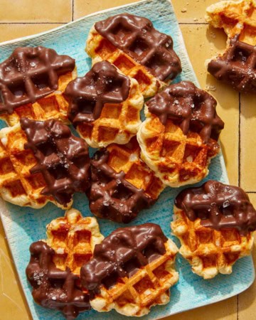 Liege waffles dipping in chocolate on a platter with one eaten on the side.