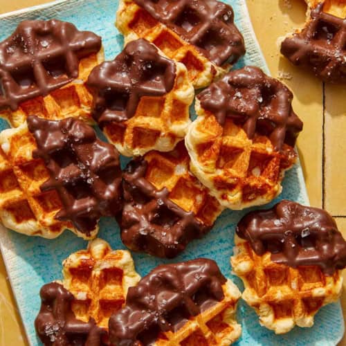 Liege waffles dipping in chocolate on a platter with one eaten on the side.