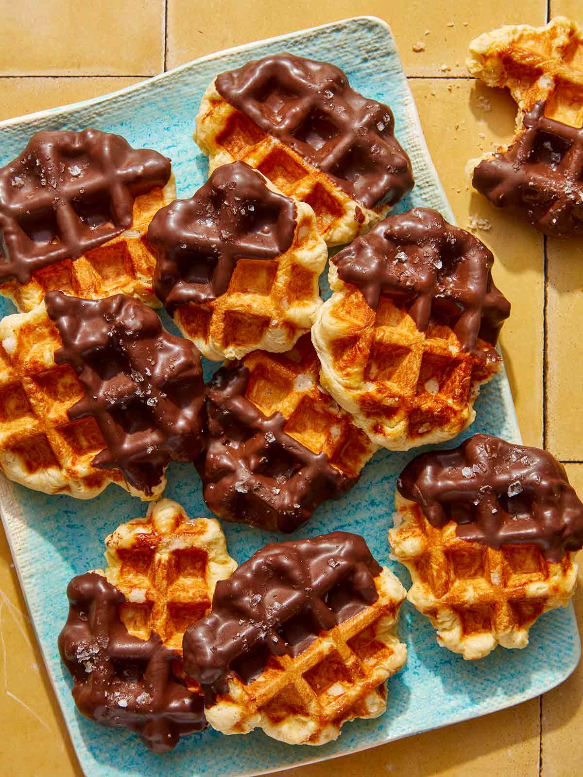 Liege waffles dipping in chocolate on a platter with one eaten on the side.