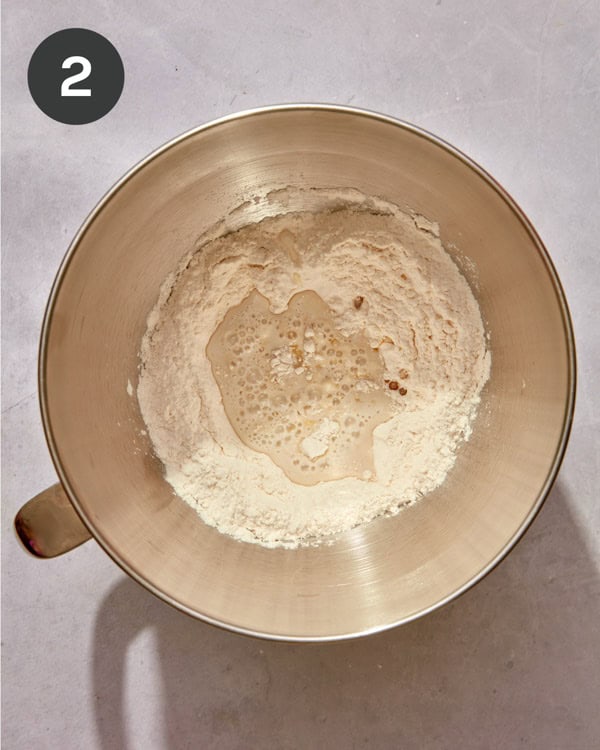 A stand mixer bowl filled with flour and a yeast mixture.