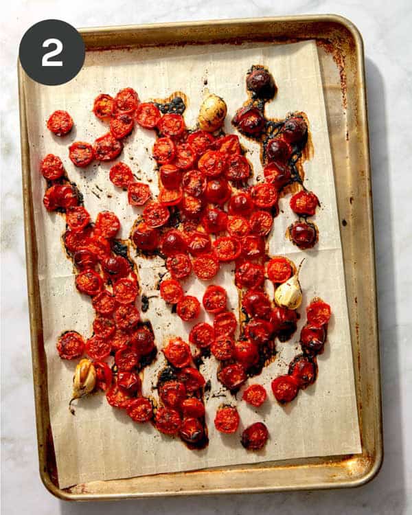 Roasted tomatoes and garlic on a baking sheet with parchment.