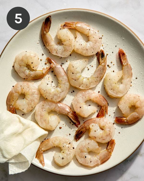 Shrimp patted dry and seasoned with salt and pepper on a plate.