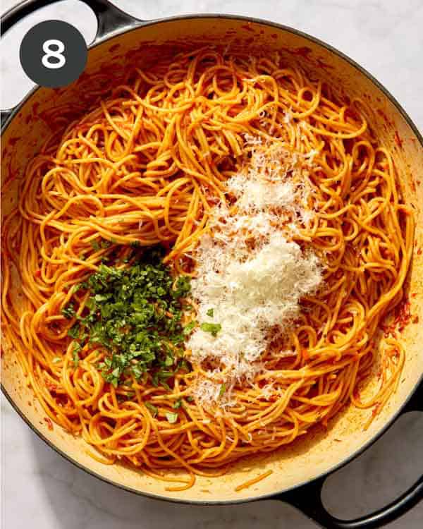 Tomato sauce spaghetti in a skillet with herbs and cheese about to be tossed together.