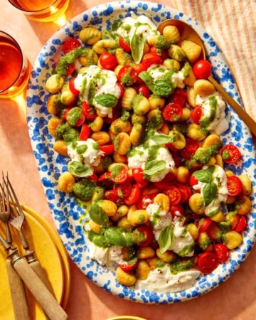 Caprese gnocchi on a platter with serving dishes on the side.
