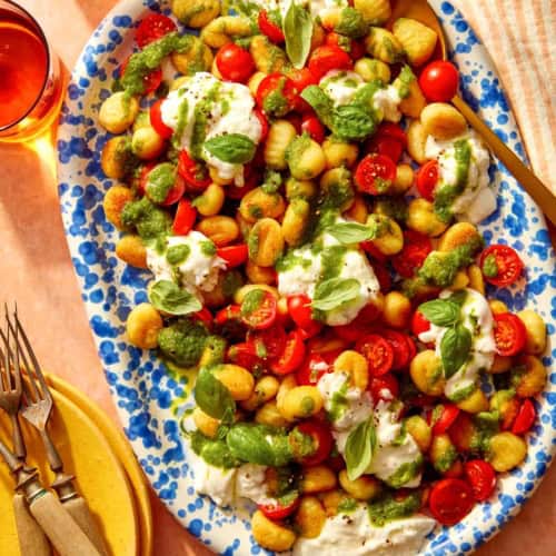 Caprese gnocchi on a platter with serving dishes on the side.