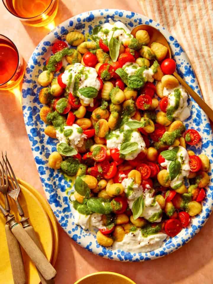 Caprese gnocchi on a platter with serving dishes on the side.