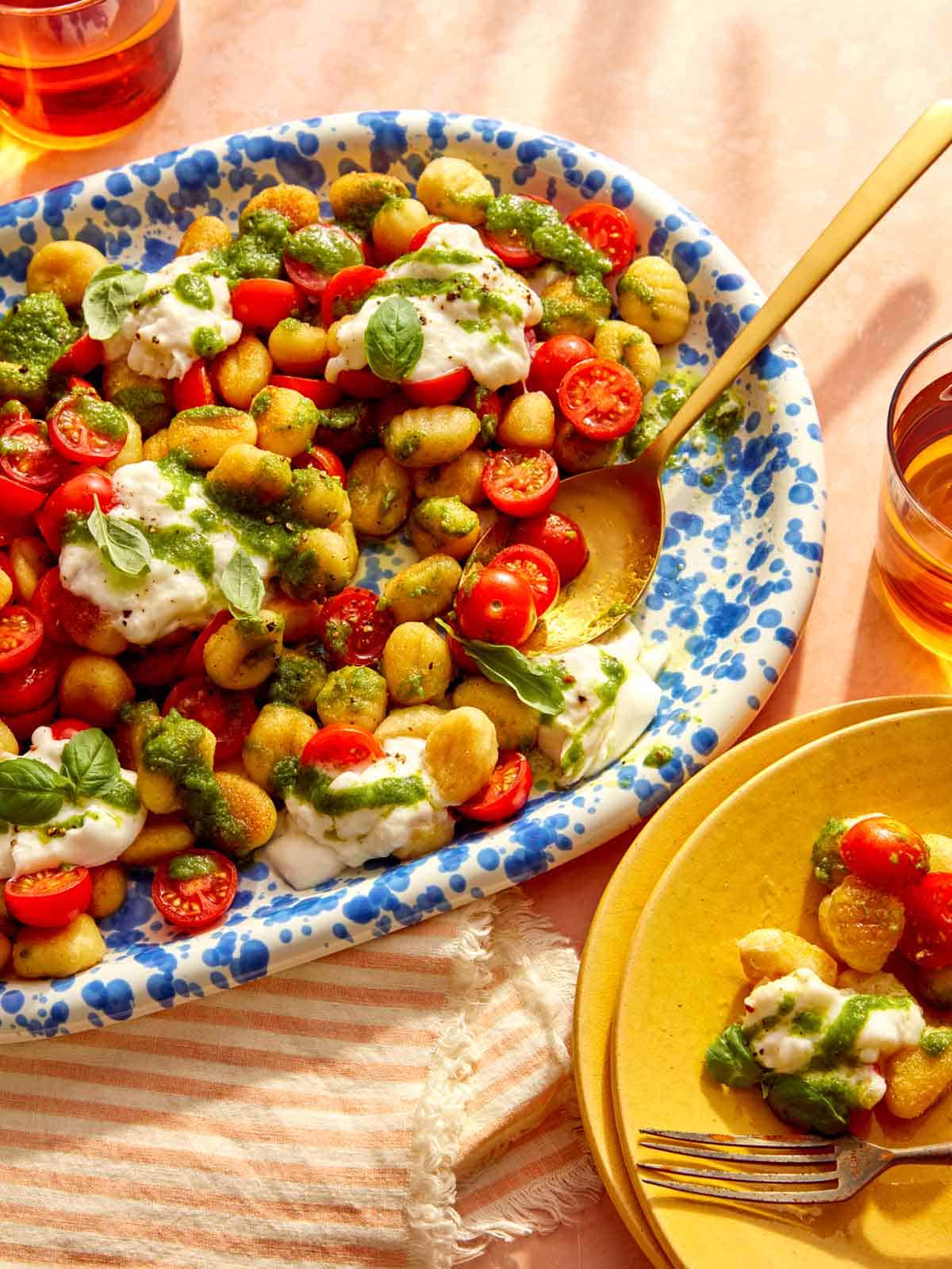 Caprese gnocchi that was pan fried on a platter with some being served onto plates.