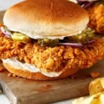 Pork Tenderloin sandwich on a cutting board with potato chips.