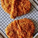 Pork cutlets on a cutting board with toppings next to it.