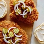 Building a pork tenderloin sandwich with pickles and onions on top of the cutlet.
