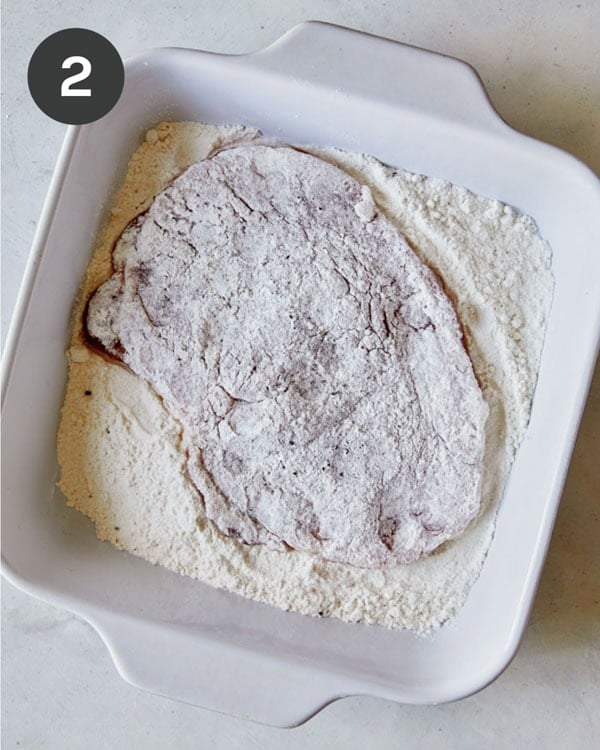 Pork tenderloin in a baking dish of flour.