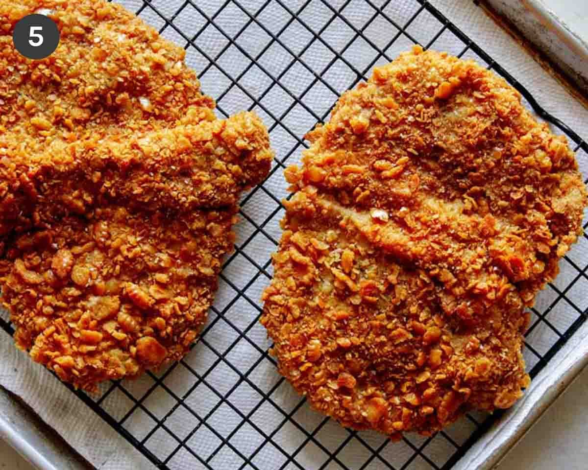Freshly fried pork tenderloin cutlets on a baking sheet.