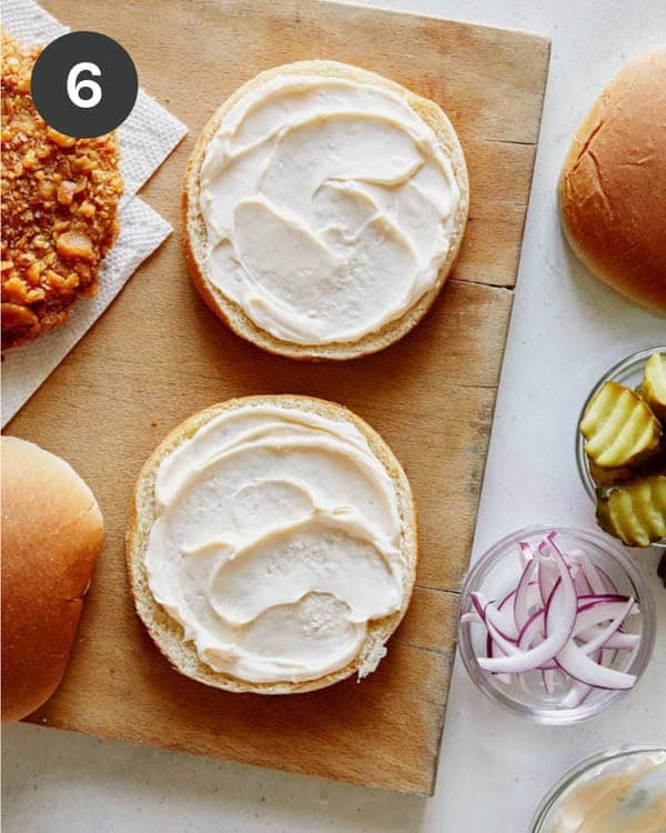 Two buns with mayonnaise spread on them and pork cutlets next to them.