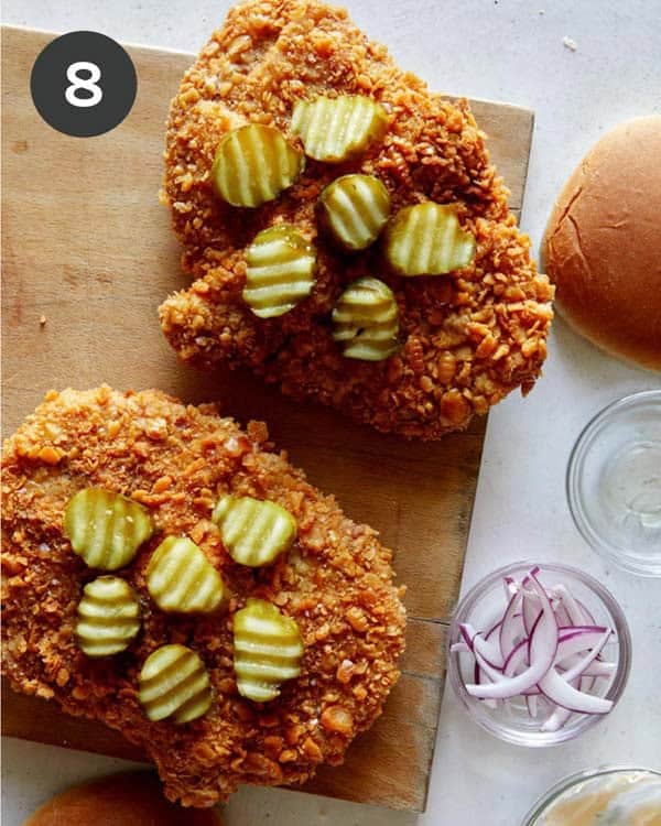 Building a pork tenderloin sandwich with pickles on top of the cutlet.