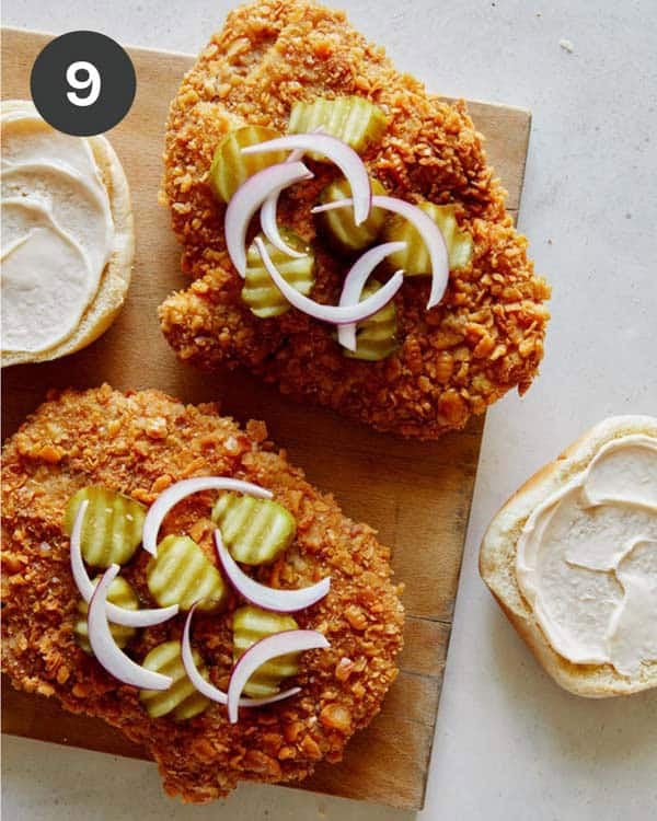 Building a pork tenderloin sandwich with pickles and onions on top of the cutlet.