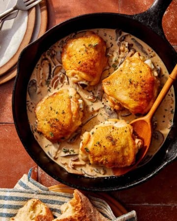 Crispy chicken thighs in a skillet with a creamy mushroom sauce.
