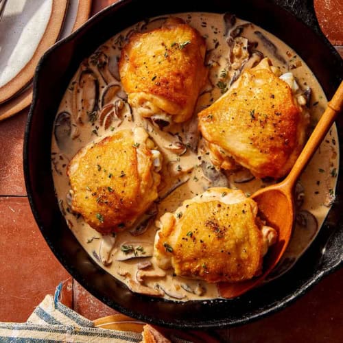 Crispy chicken thighs in a skillet with a creamy mushroom sauce.