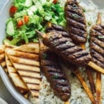 Lamb kofta skewers on a platter with pita and rice.